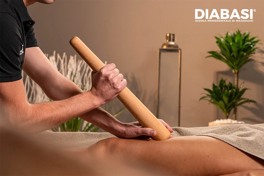 Operatore esegue la tecnica del Massaggio Maori con bastone in legno su coscia durante un trattamento muscolare profondo. Diabasi Scuola Professionale di Massaggio.