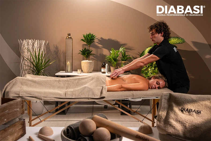 Operatore esegue una seduta di Massaggio Maori su cliente sdraiata su lettino in ambiente professionale con strumenti in legno visibili. Diabasi Scuola Professionale di massaggio.