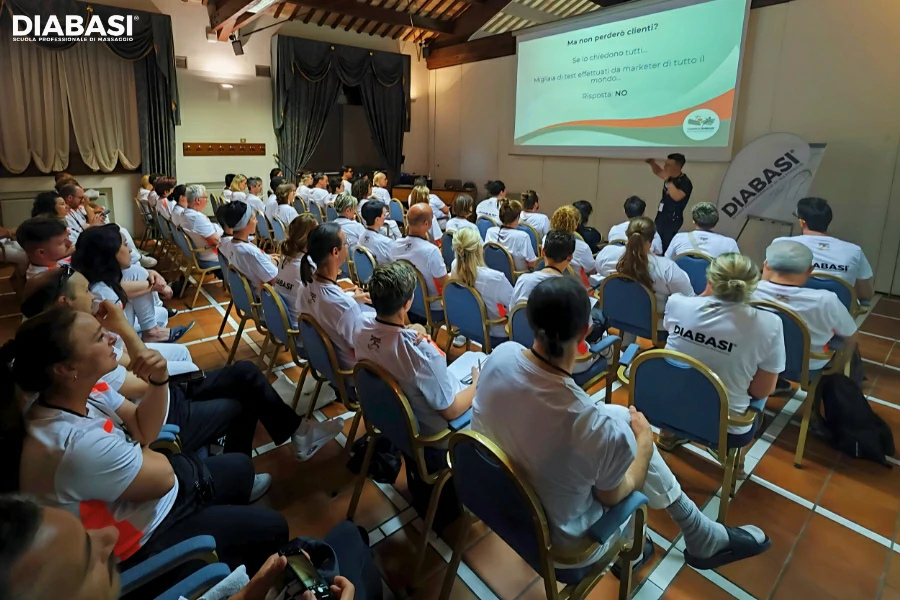 Marco Fraccalvieri spiega come strutturare una strategia di marketing per massaggiatori davanti a una lavagna con canali Google e Meta. Diabasi Scuola Professionale di Massaggio