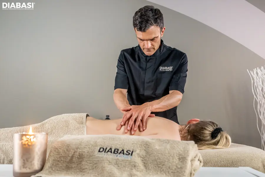 Un massaggiatore professionista esegue la manovra di impastamento (petrissage) sulla schiena di una cliente durante una seduta di massaggio base svedese Metodo DIABASI.
