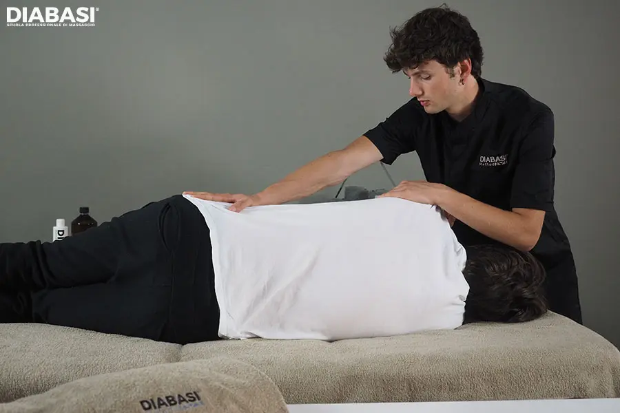 Un professionista della Scuola Professionale Diabasi esegue una tecnica di massaggio posturale in decubito laterale, agendo sulle catene muscolari della schiena e della spalla per correggere gli squilibri dell'assetto corporeo.