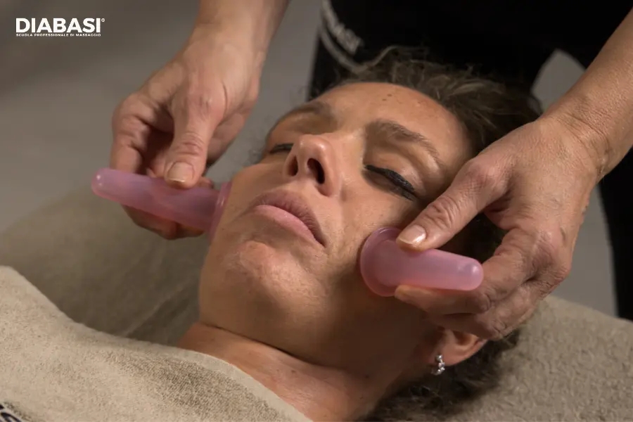 Trattamento di face cupping dinamico con coppette in silicone rosa durante il massaggio viso lifting.