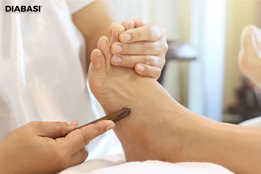 Operatrice olistica applica lo stickwood tradizionale di legno scuro sul profilo laterale del piede durante una seduta di Thai Foot Massage.