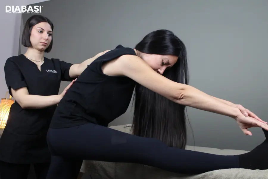 Operatrice professionista esegue esercizi stretching funzionale della catena posteriore e dei muscoli ischiocrurali su una cliente. Diabasi scuola professionale di massaggio