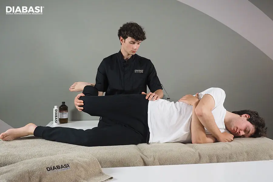 Massaggiatore professionista esegue esercizi stretching passivo dell'anca su un cliente in decubito laterale sul lettino.